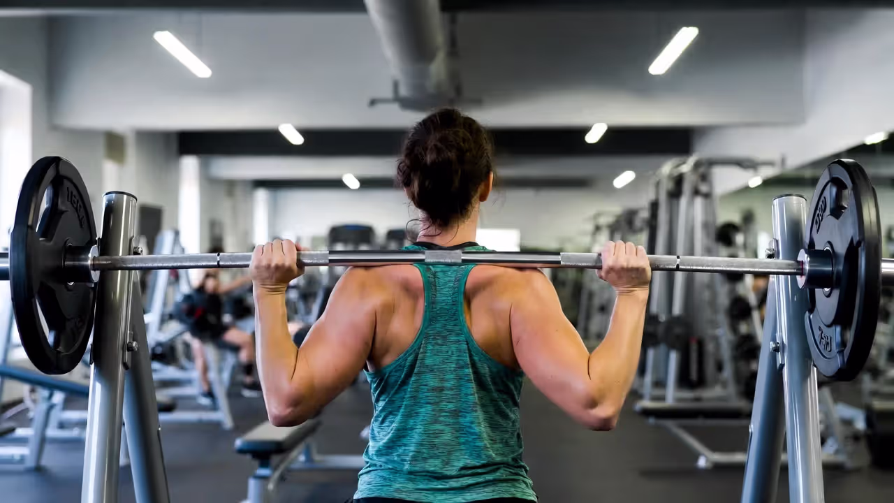 Person performing a barbell squat or deadlift with controlled form in a gym