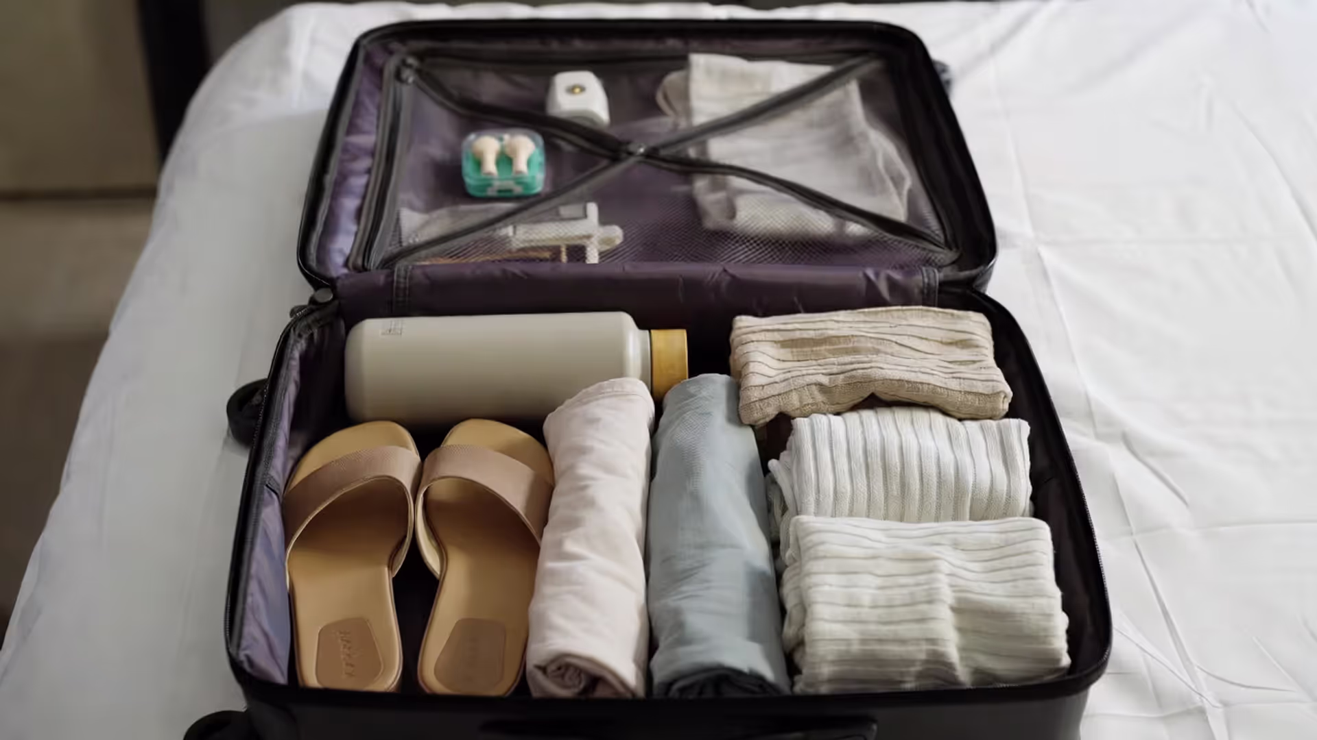 Open suitcase packed with yoga retreat essentials including headlamp, earplugs, water bottle, and practice clothes.